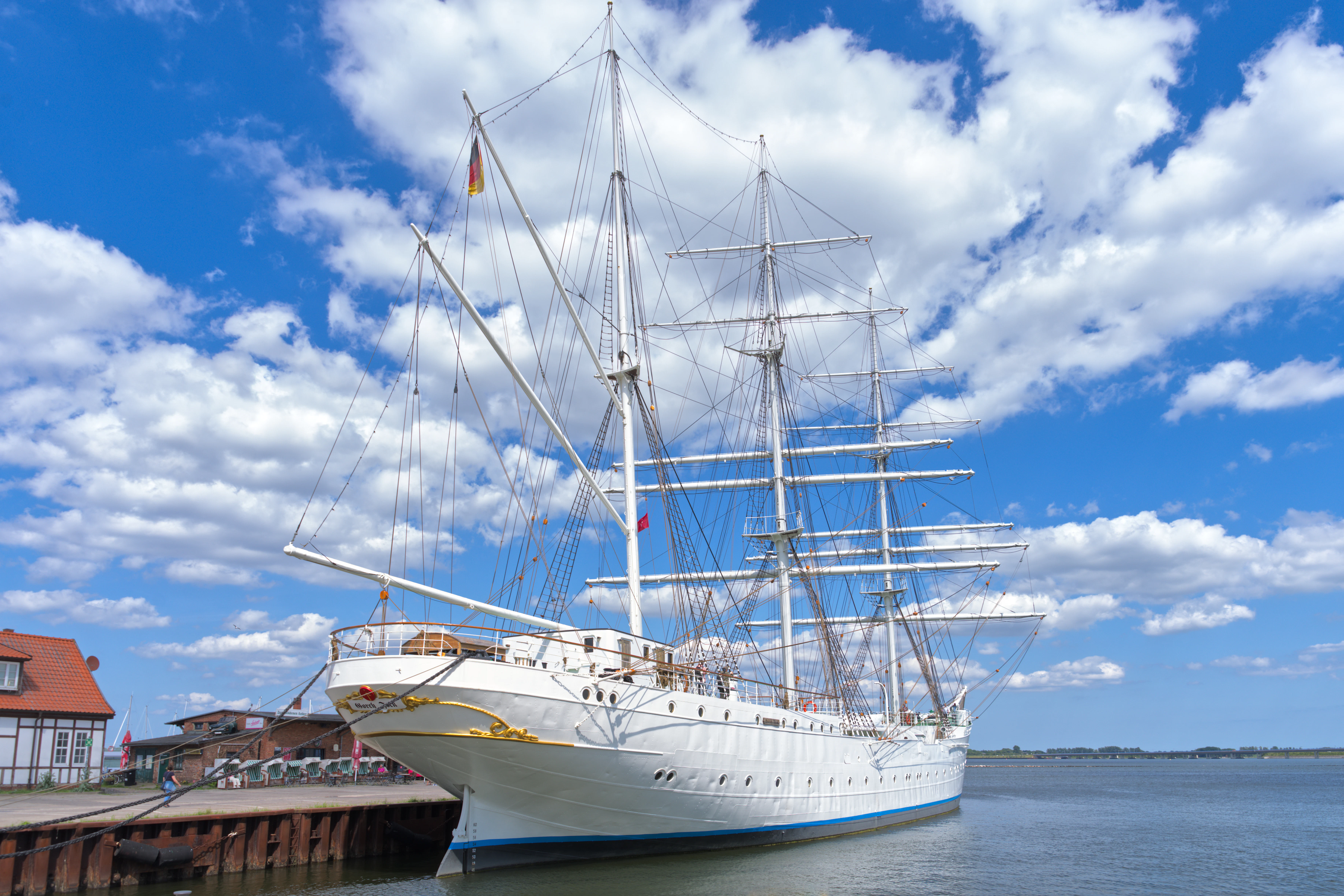 White sailing ship docked under a cloudy blue sky