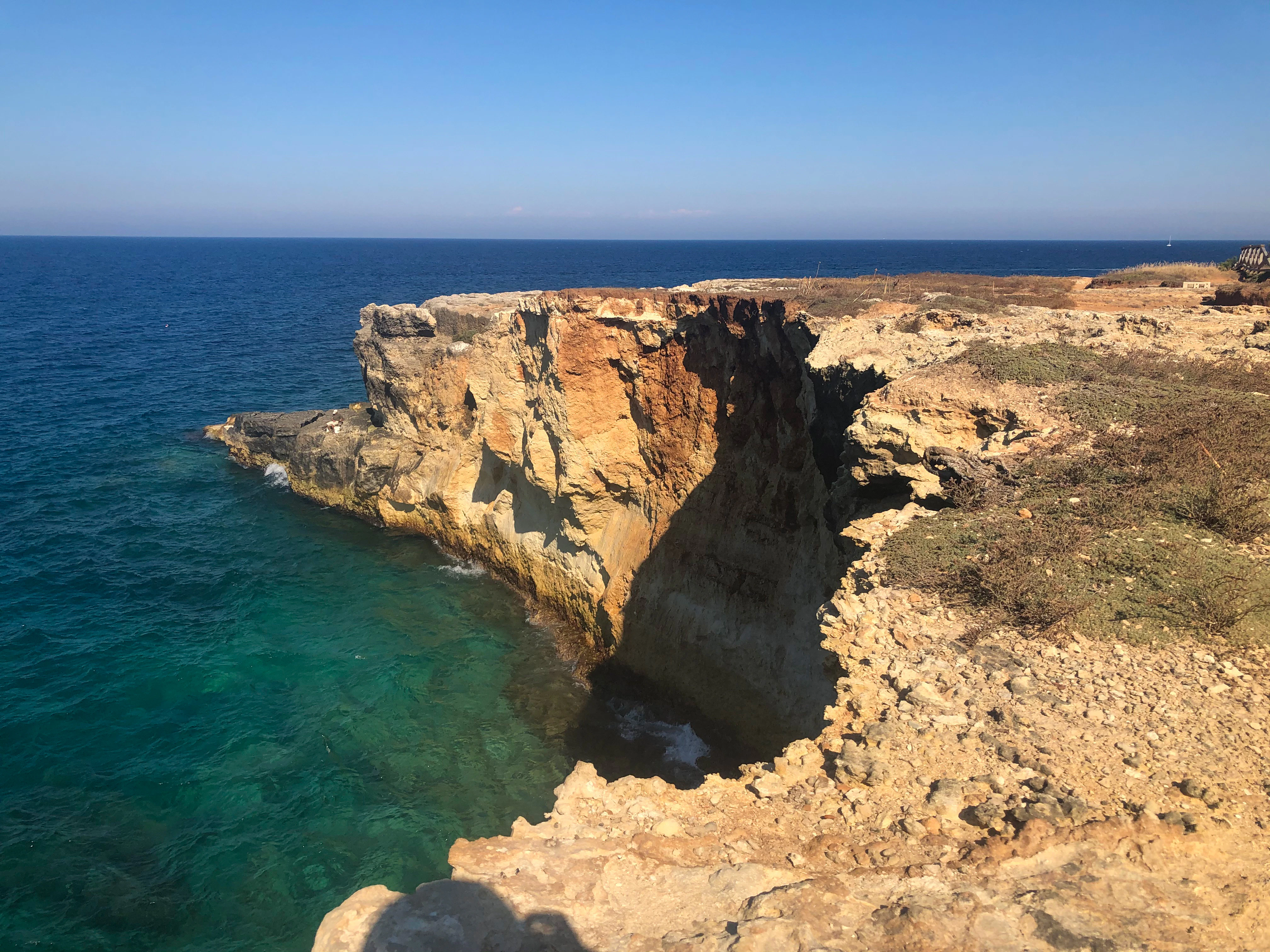 a rocky cliff overlooks the ocean on a sunny day
