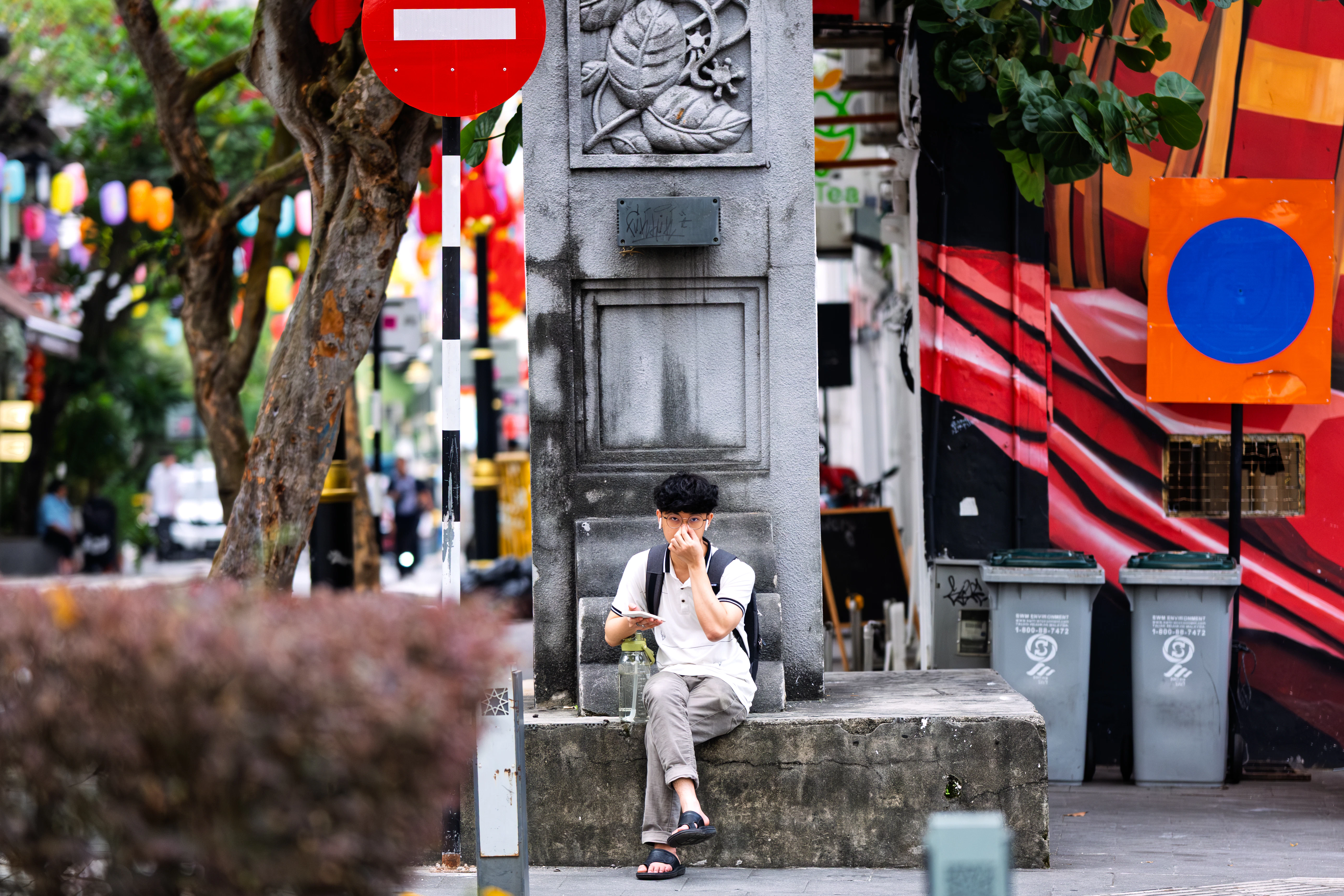 Young man sitting on a ledge near a street.