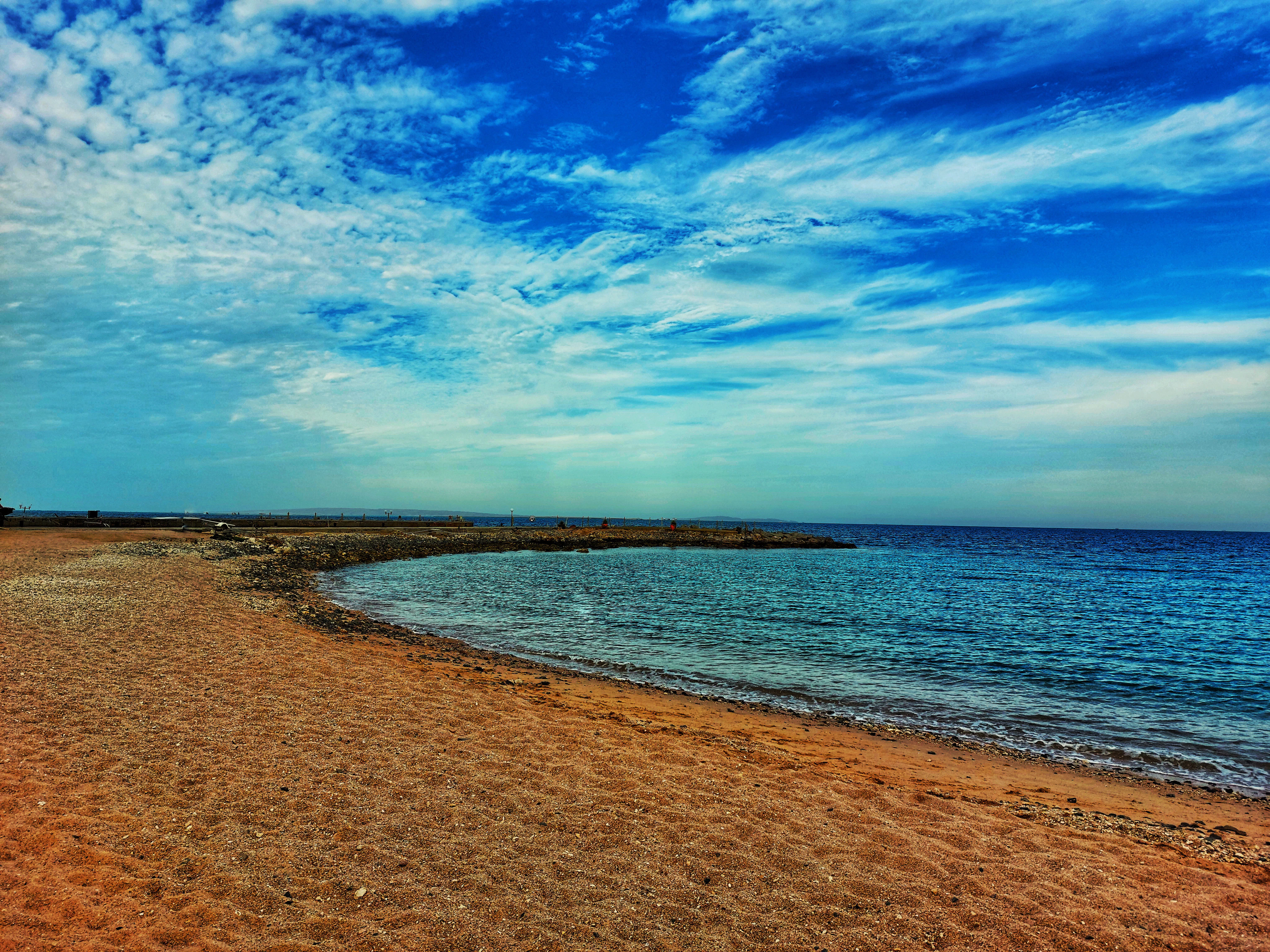 a sandy beach next to the ocean under a blue sky