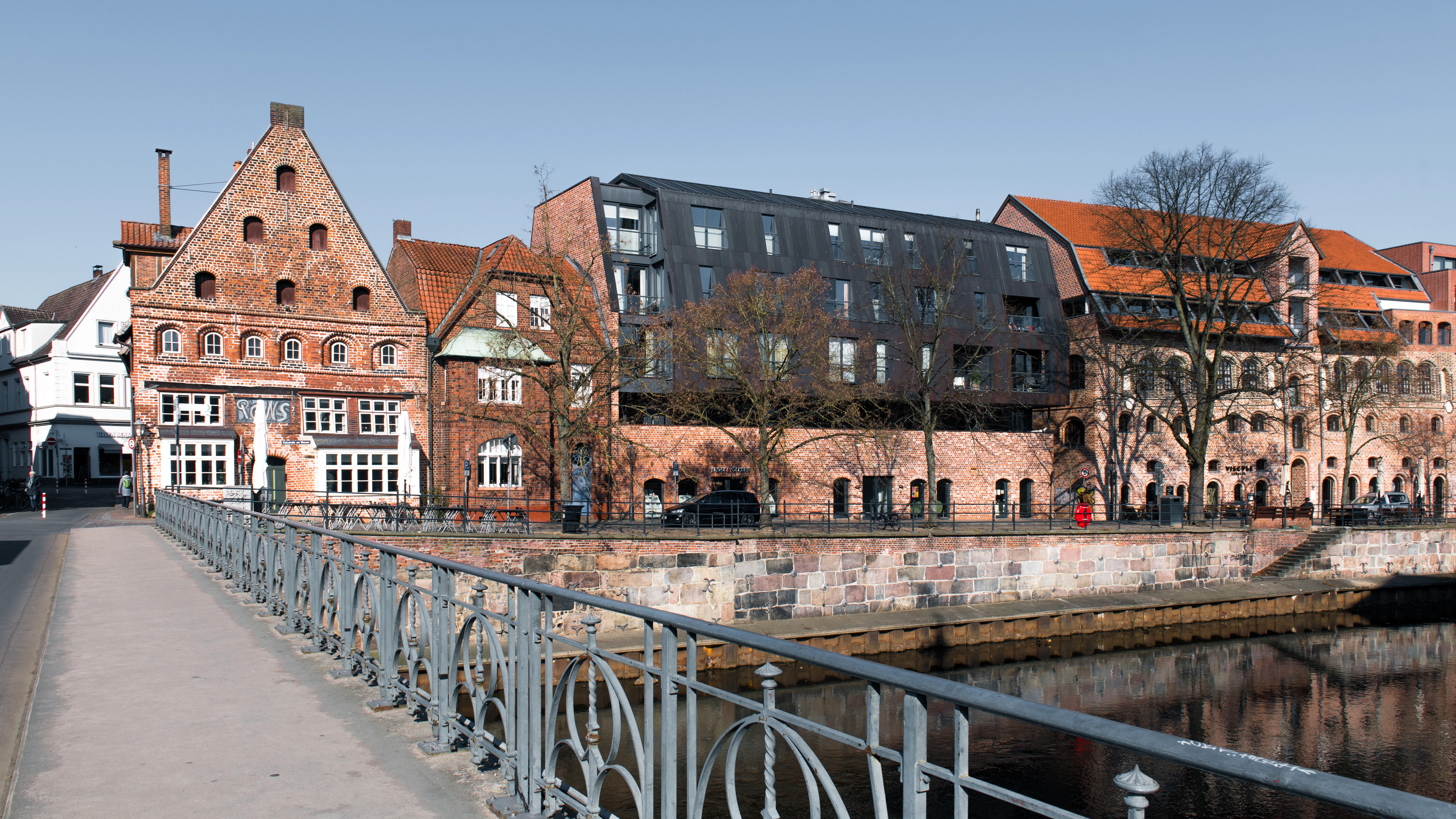 Historic buildings line a river with a bridge in foreground