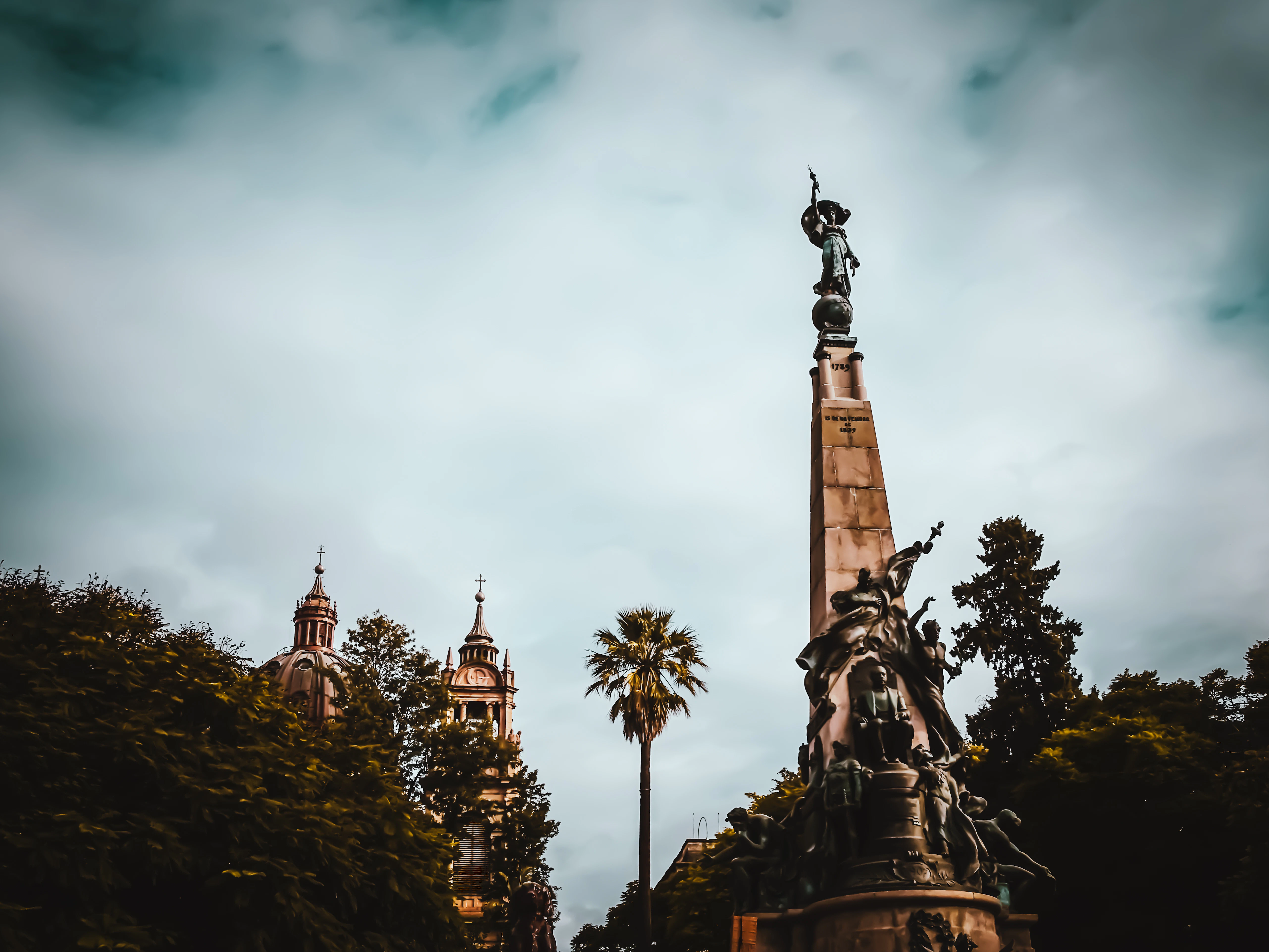 a statue on a hill with trees and a building in the background