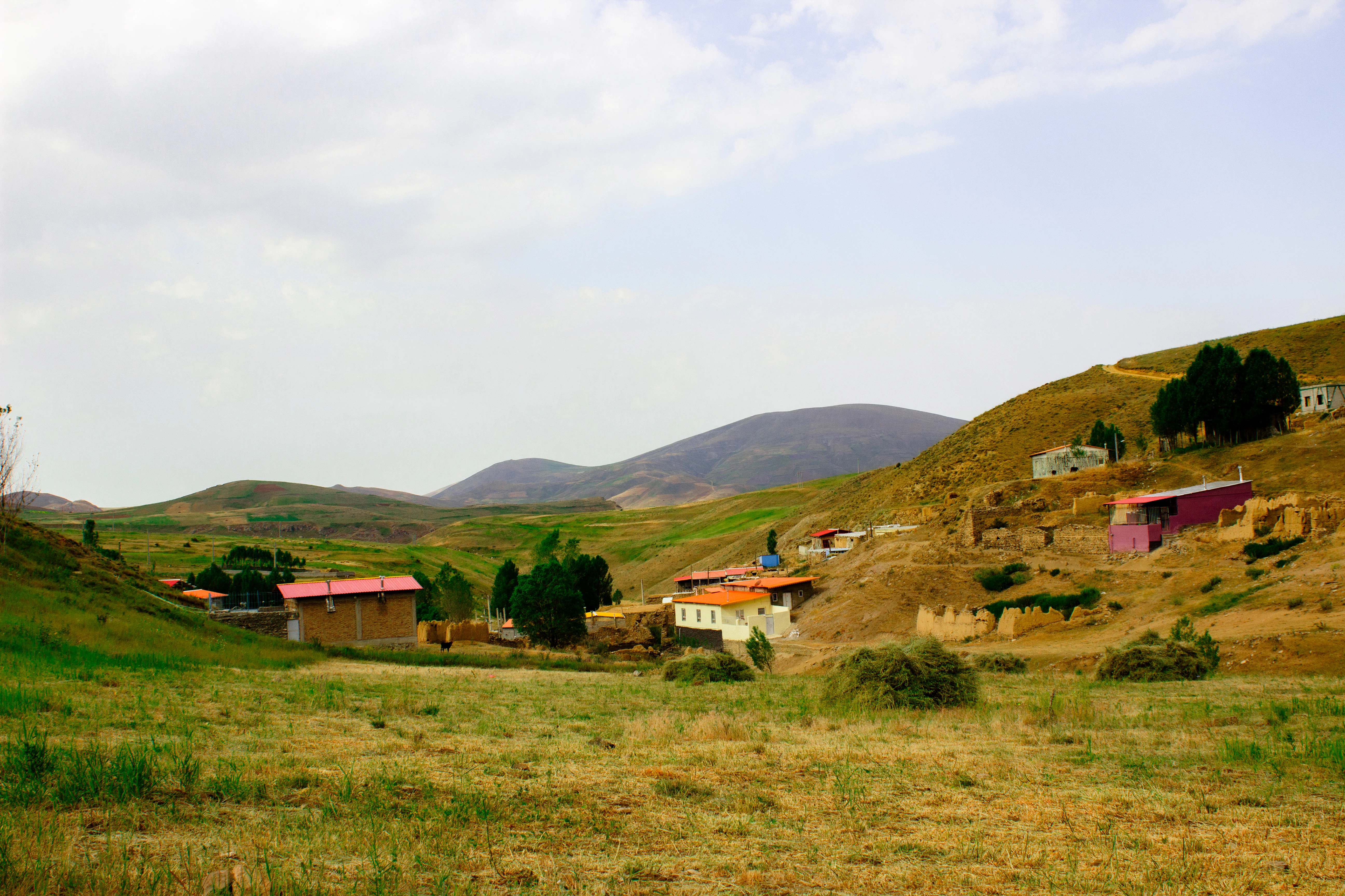 Rural village nestled in rolling hills under a cloudy sky.