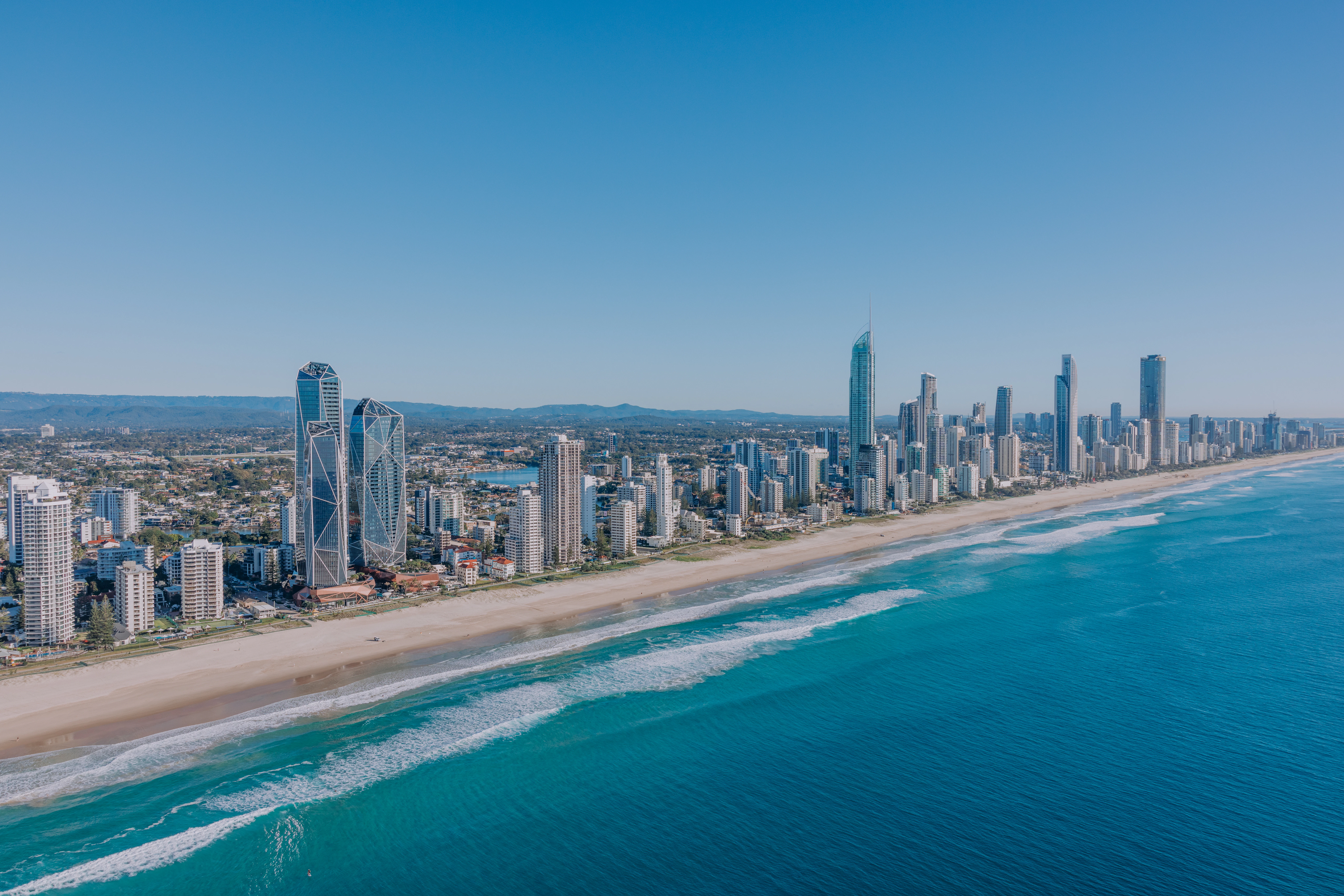Modern skyscrapers line a sandy beach next to ocean.