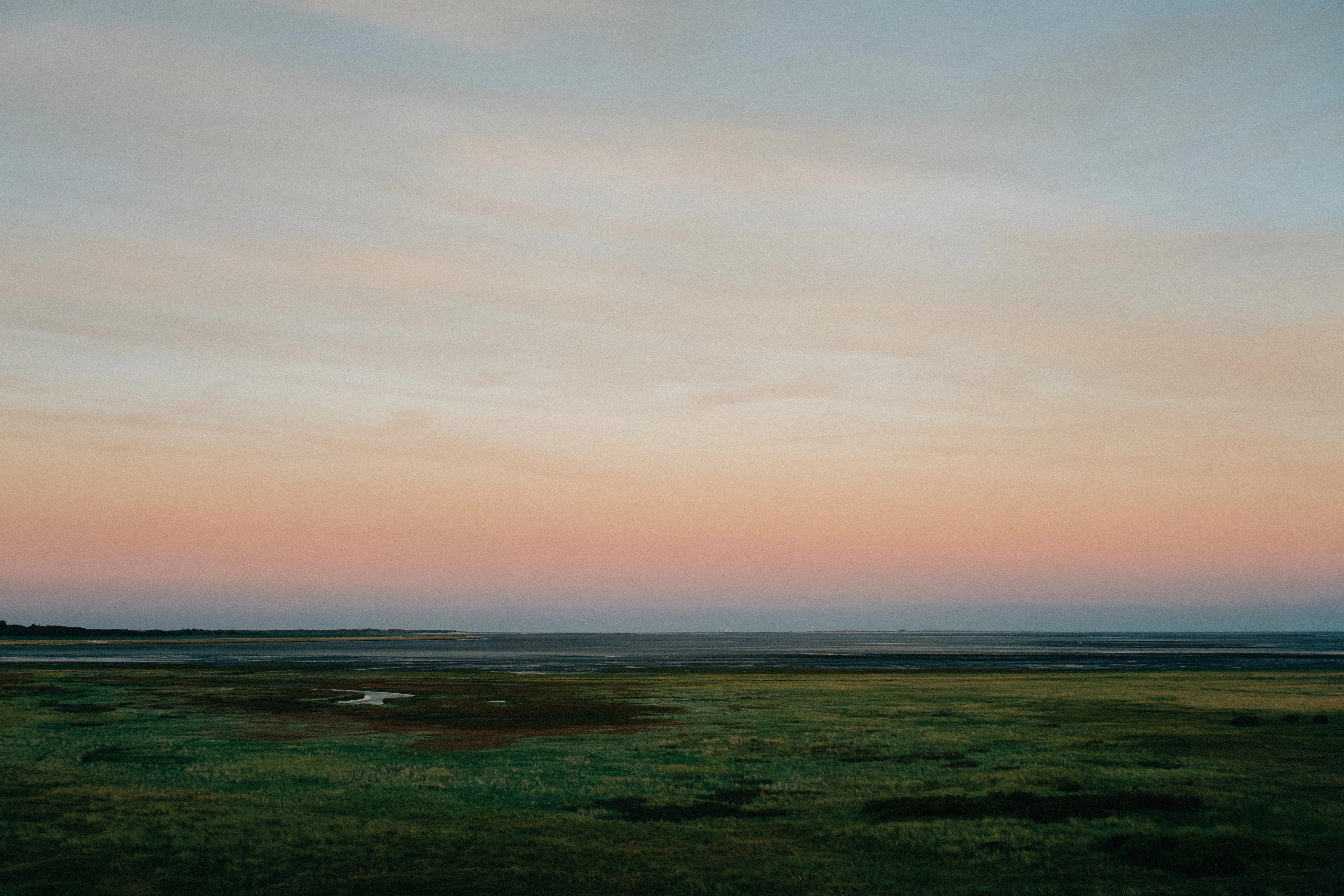 Pastel sunset over a grassy field and water