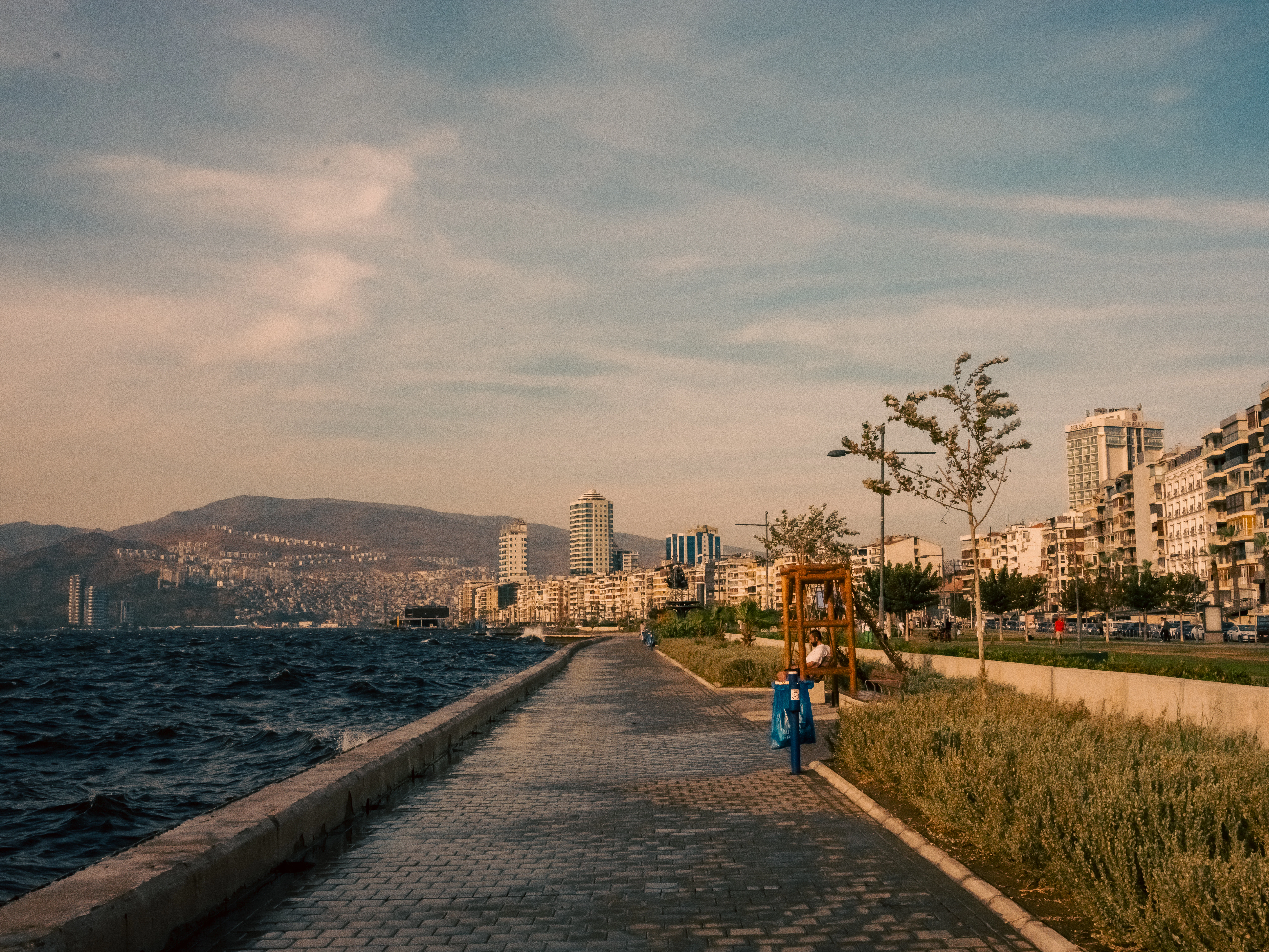 Seaside promenade with city buildings and distant hills.