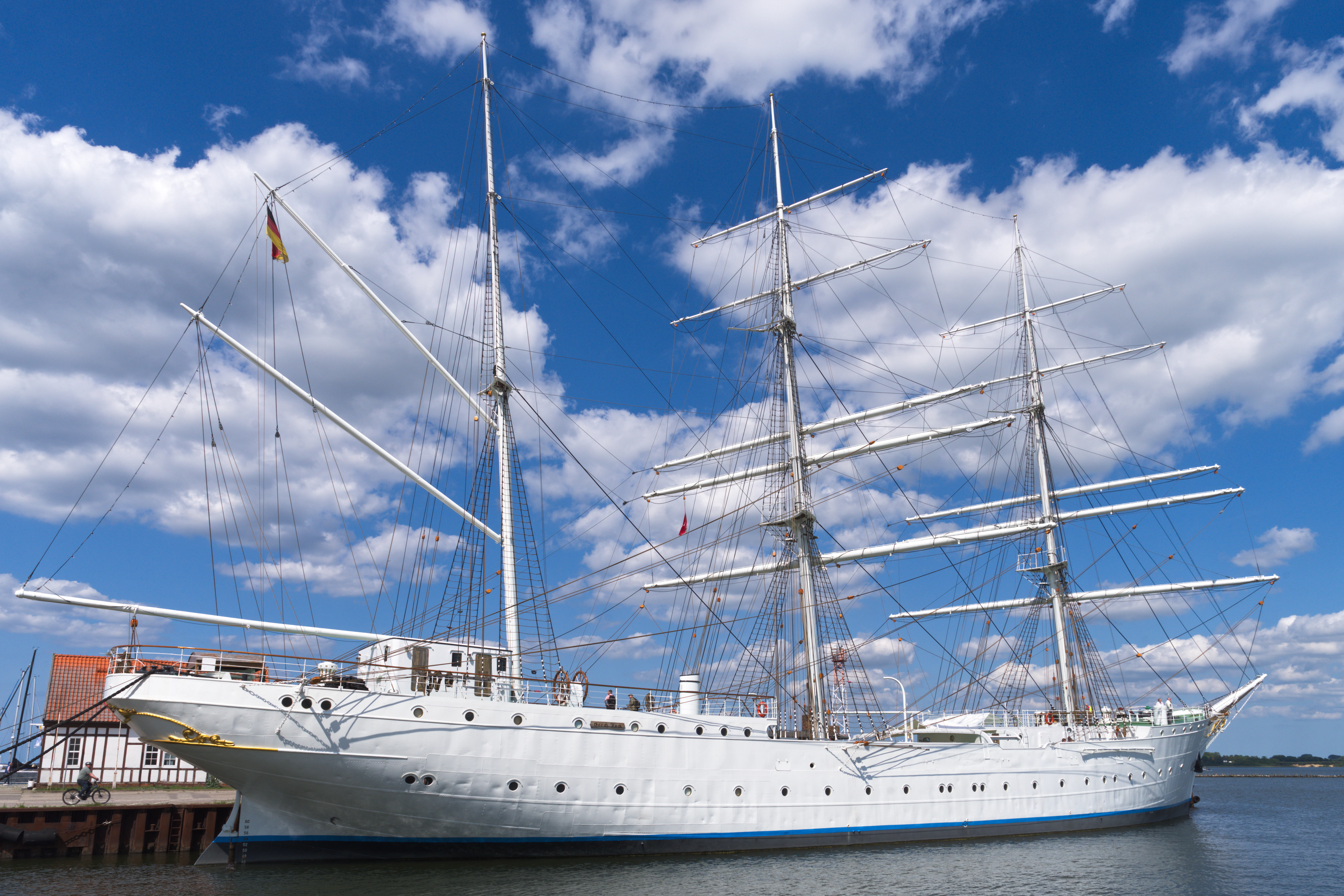 A large white sailing ship docked under a blue sky.