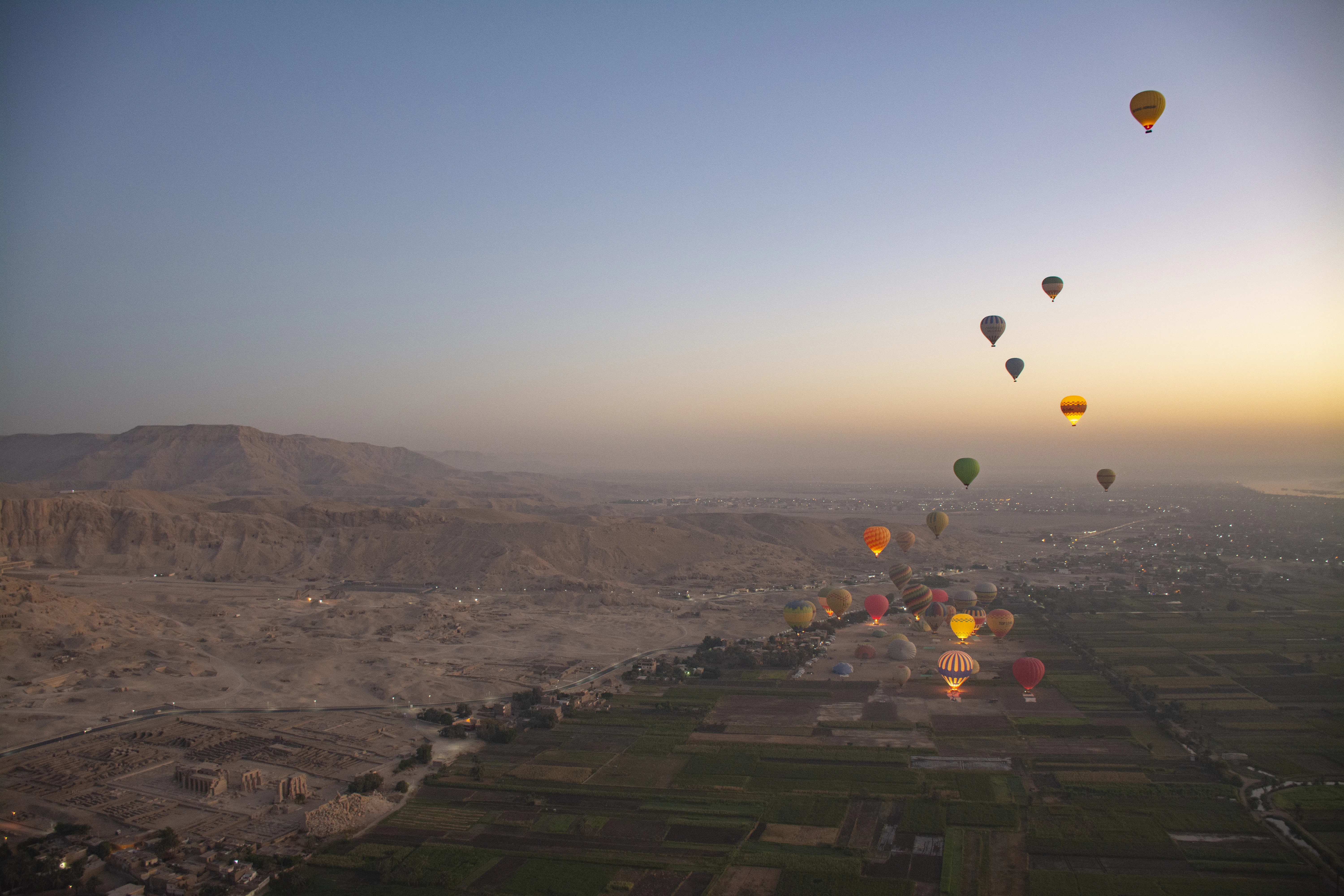 Hot air balloons float over a river valley at sunrise.